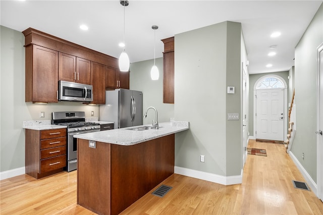 kitchen featuring sink, hanging light fixtures, light hardwood / wood-style flooring, kitchen peninsula, and stainless steel appliances