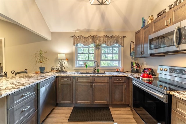 kitchen with sink, light hardwood / wood-style flooring, vaulted ceiling, appliances with stainless steel finishes, and kitchen peninsula