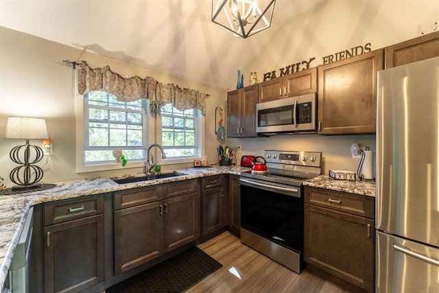 kitchen featuring light stone countertops, sink, stainless steel appliances, an inviting chandelier, and light hardwood / wood-style flooring