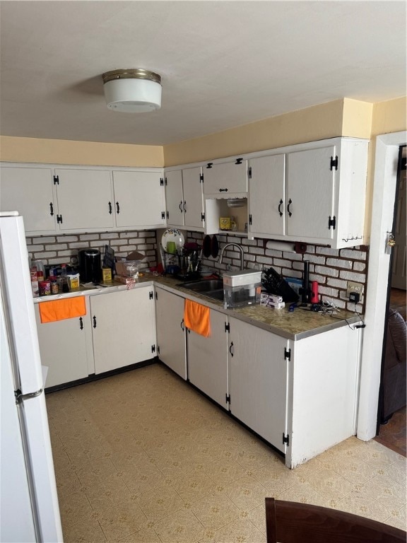 kitchen with tasteful backsplash, white cabinetry, sink, and white fridge