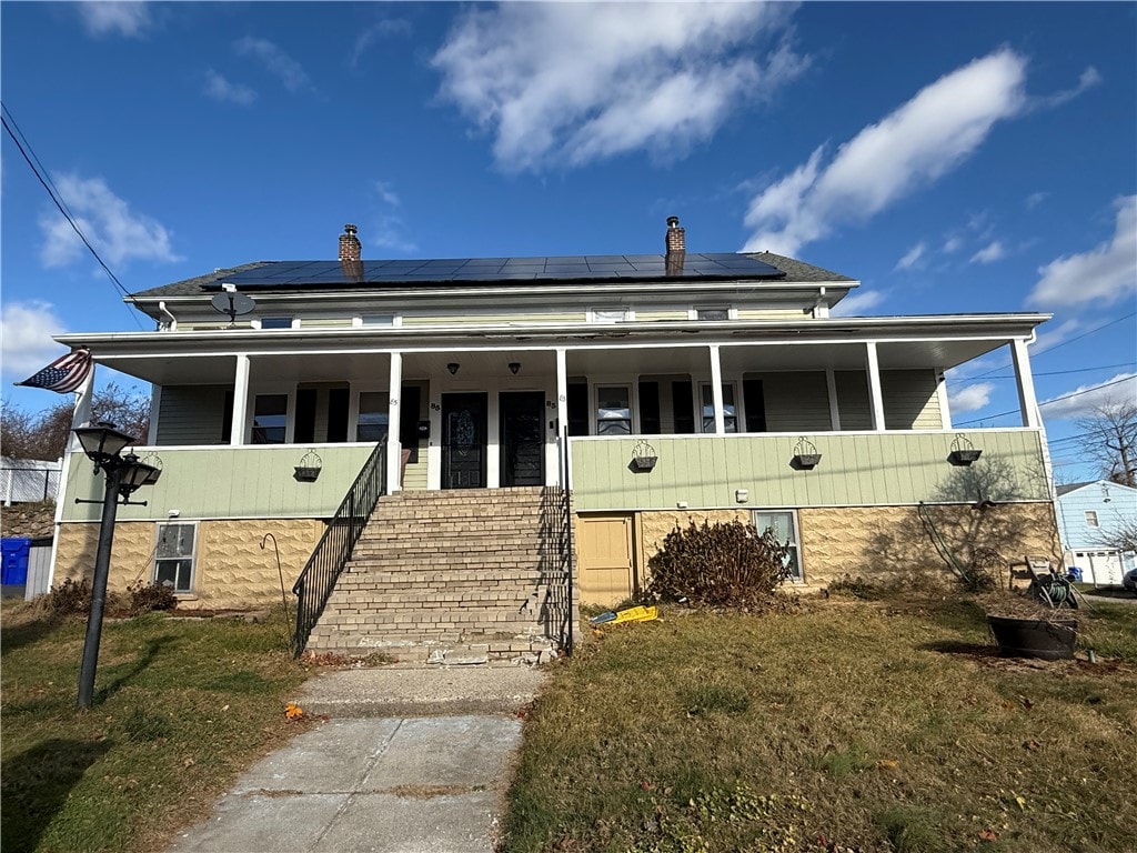 view of front of house featuring a front yard, a porch, and solar panels