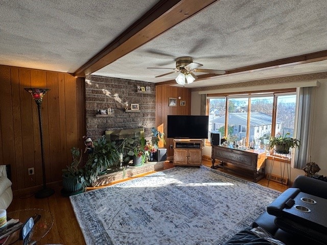 living room featuring ceiling fan, wood walls, wood-type flooring, and a textured ceiling