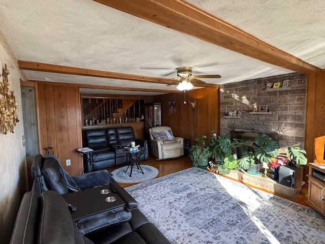 living room with wooden walls, ceiling fan, a textured ceiling, beam ceiling, and wood-type flooring