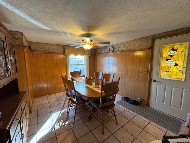 tiled dining space featuring wooden walls, ceiling fan, and a textured ceiling