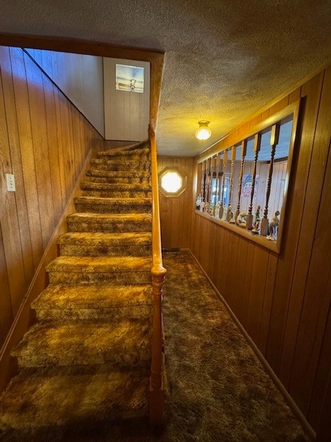 stairway with carpet flooring, a textured ceiling, and wooden walls