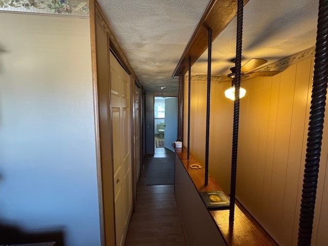 hallway with dark hardwood / wood-style floors, wood walls, and a textured ceiling