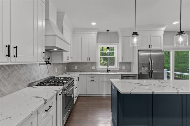 kitchen featuring white cabinets, custom range hood, stainless steel appliances, and hanging light fixtures