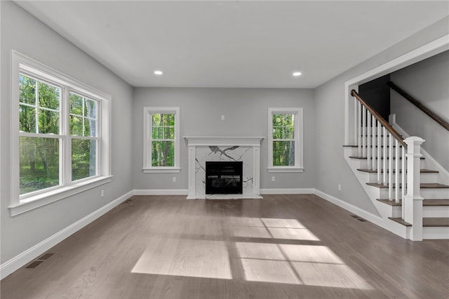 unfurnished living room with hardwood / wood-style floors, a high end fireplace, and a healthy amount of sunlight