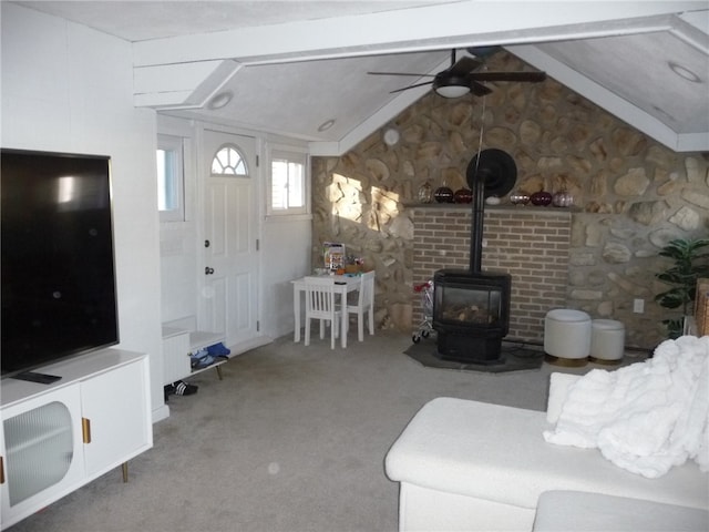 living room with a wood stove, ceiling fan, carpet, and vaulted ceiling with beams