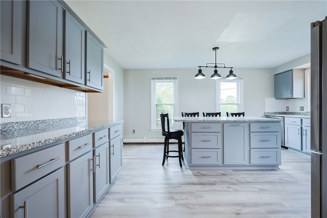 kitchen with pendant lighting, light hardwood / wood-style floors, light stone counters, and gray cabinets