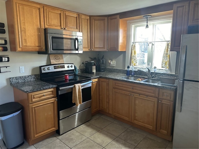 kitchen featuring sink, stainless steel appliances, dark stone counters, decorative light fixtures, and light tile patterned floors