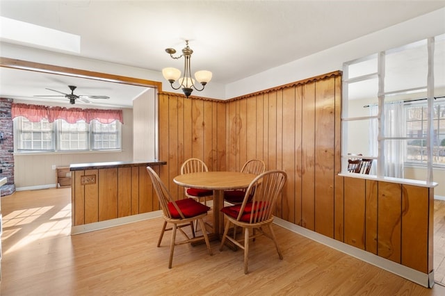 dining space featuring ceiling fan with notable chandelier, light wood-type flooring, and wooden walls