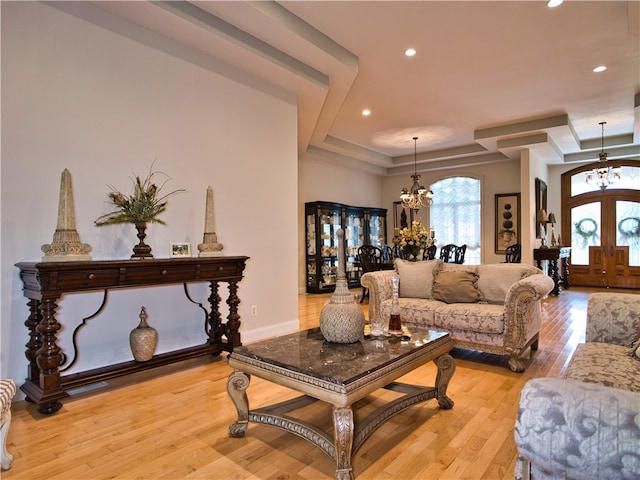 living room with a tray ceiling, light hardwood / wood-style flooring, french doors, and an inviting chandelier