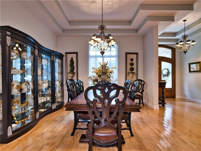 dining area featuring light wood-type flooring, a raised ceiling, plenty of natural light, and a notable chandelier