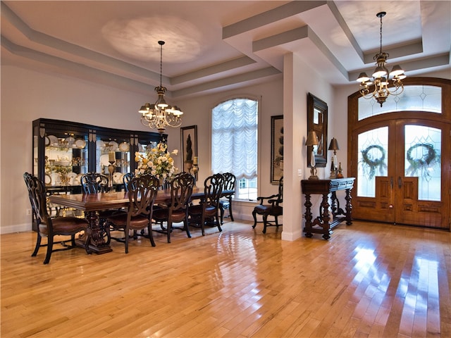 dining space with an inviting chandelier, a raised ceiling, french doors, and light hardwood / wood-style flooring