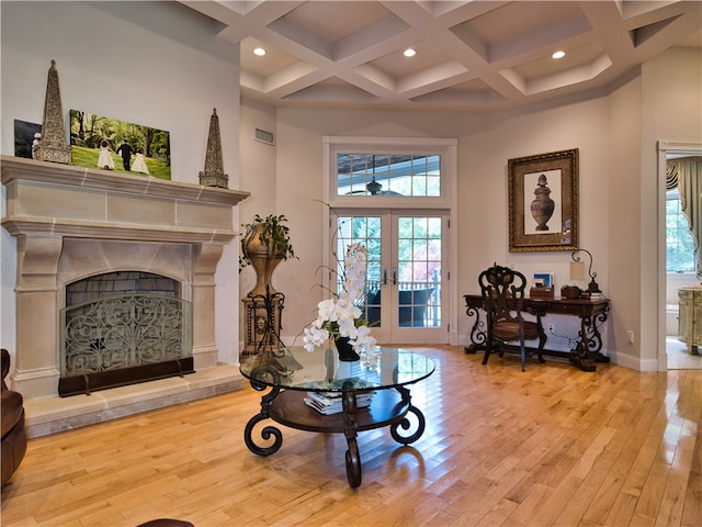 living area featuring french doors, coffered ceiling, beamed ceiling, a towering ceiling, and light hardwood / wood-style floors