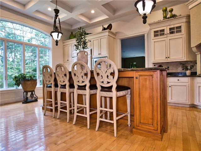 kitchen featuring pendant lighting, cream cabinets, coffered ceiling, light wood-type flooring, and beam ceiling