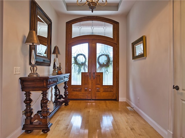 entryway featuring a tray ceiling, french doors, light hardwood / wood-style floors, and a notable chandelier