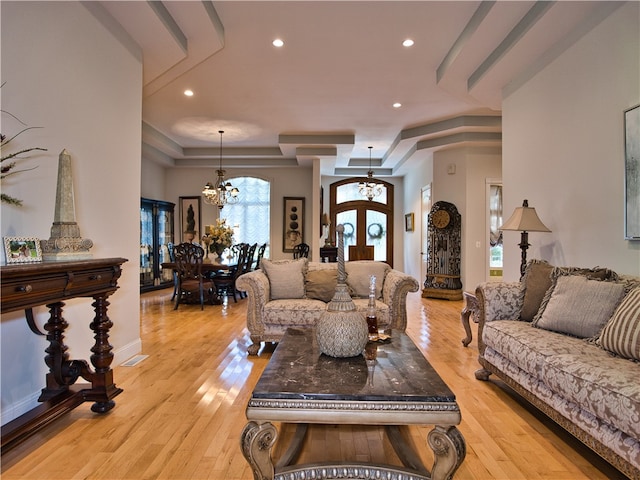 living room with an inviting chandelier, a raised ceiling, french doors, and light hardwood / wood-style flooring