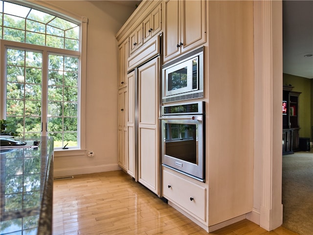 kitchen with a healthy amount of sunlight, light hardwood / wood-style floors, dark stone counters, and cream cabinets