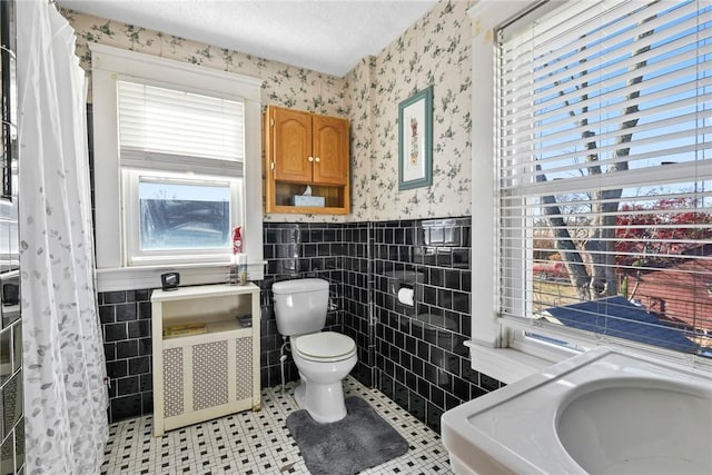 bathroom featuring tile patterned flooring, toilet, tile walls, and a textured ceiling