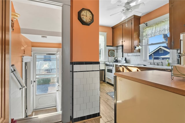 kitchen featuring stainless steel gas stove, ceiling fan, light wood-type flooring, and sink