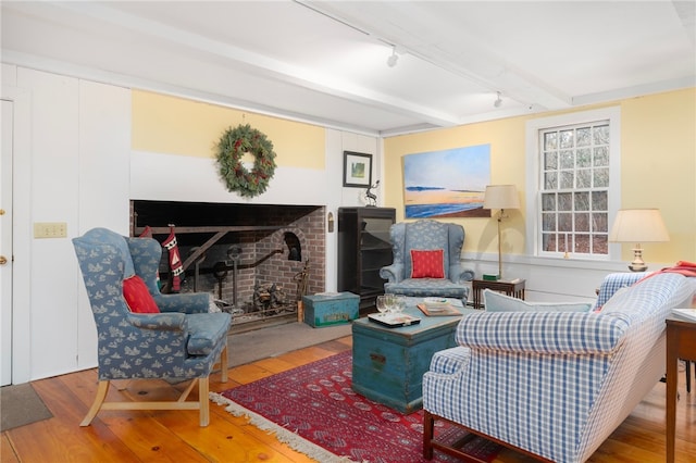 living area featuring hardwood / wood-style floors, a brick fireplace, and beam ceiling