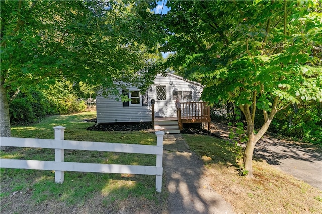 view of property hidden behind natural elements featuring a wooden deck and a front lawn