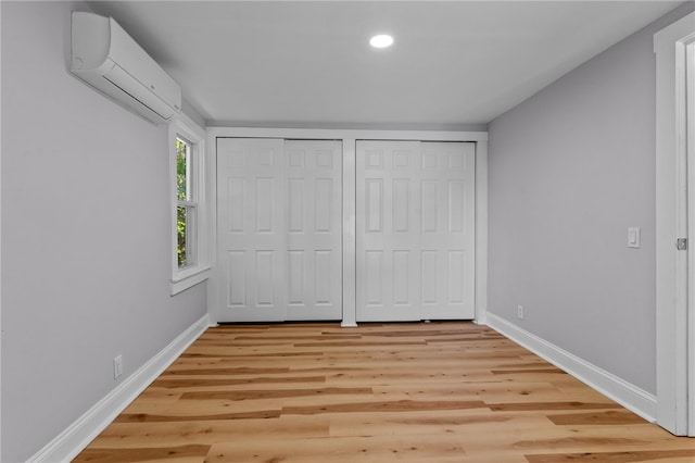 unfurnished bedroom with a wall unit AC, light hardwood / wood-style floors, and two closets