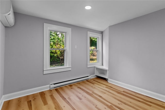 spare room with baseboard heating, a wall mounted AC, and light hardwood / wood-style flooring