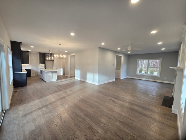 unfurnished living room featuring ceiling fan with notable chandelier and dark wood-type flooring