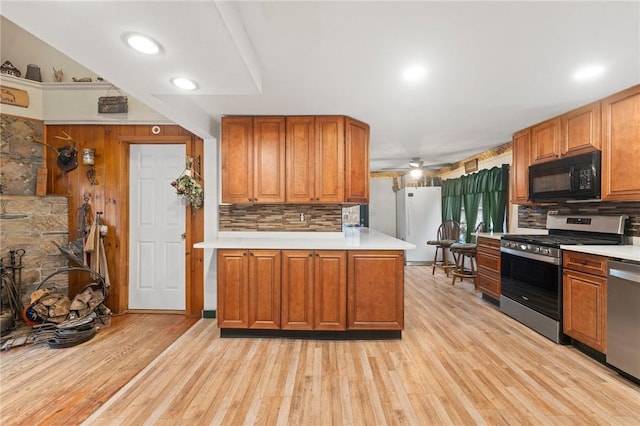 kitchen with wood walls, backsplash, ceiling fan, appliances with stainless steel finishes, and light hardwood / wood-style floors