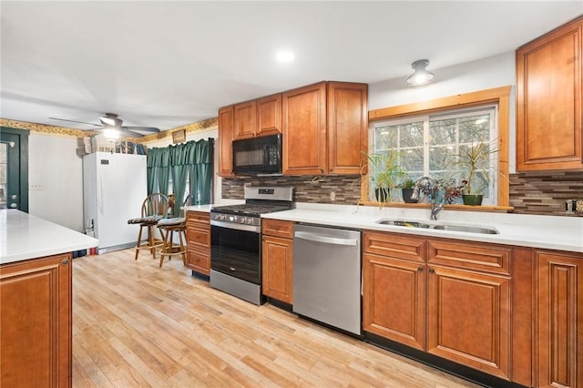 kitchen featuring ceiling fan, sink, stainless steel appliances, light hardwood / wood-style flooring, and backsplash