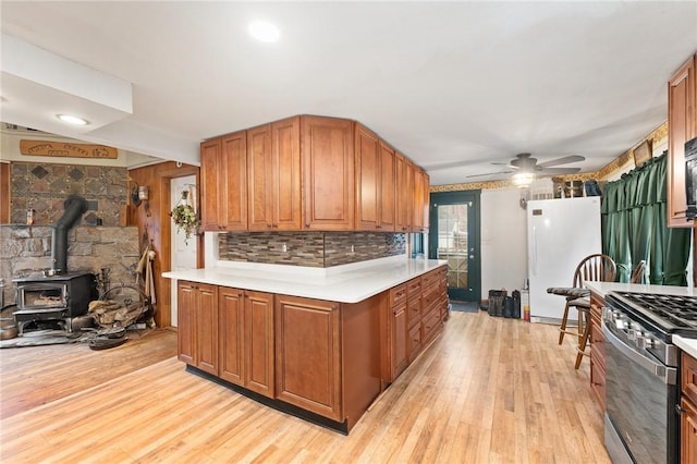 kitchen featuring a wood stove, ceiling fan, stainless steel gas stove, light hardwood / wood-style flooring, and white refrigerator