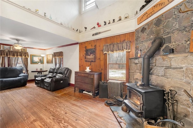 living room with radiator, ornamental molding, ceiling fan, hardwood / wood-style flooring, and a wood stove