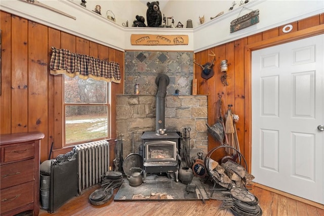 living room featuring wood walls, wood-type flooring, a wood stove, and radiator