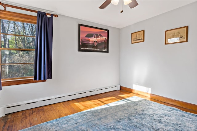 empty room with hardwood / wood-style flooring, ceiling fan, and a baseboard heating unit