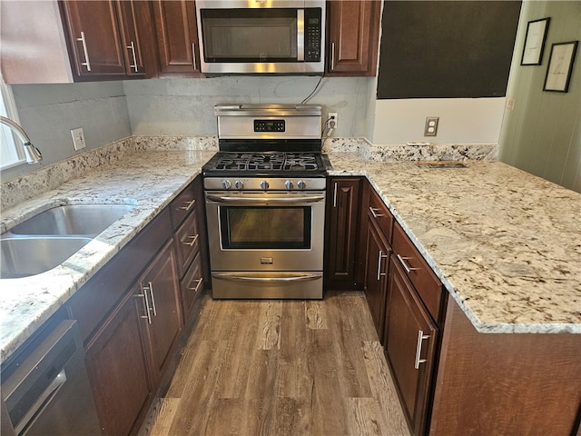 kitchen featuring appliances with stainless steel finishes, light stone counters, dark brown cabinetry, sink, and hardwood / wood-style flooring