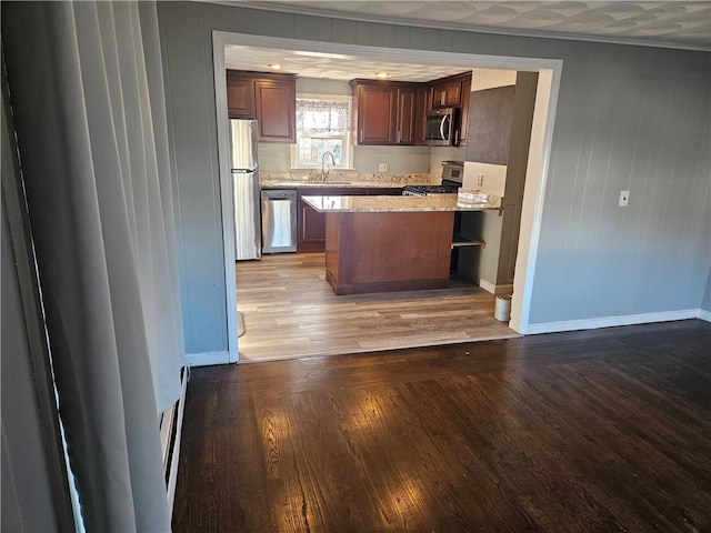 kitchen featuring light stone countertops, appliances with stainless steel finishes, ornamental molding, sink, and wood-type flooring