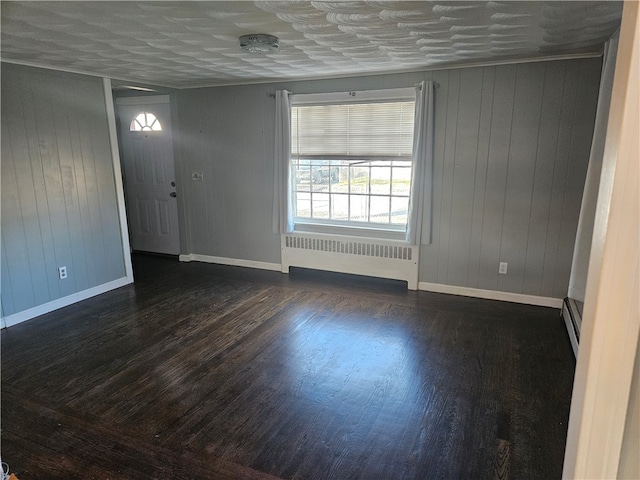 interior space with baseboard heating, radiator, wooden walls, and dark wood-type flooring