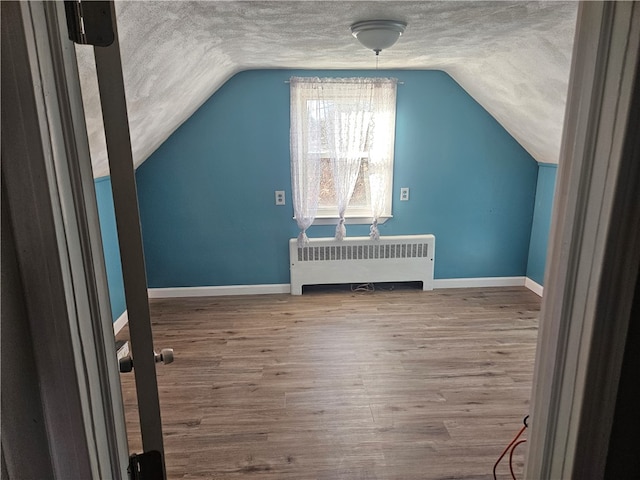 bonus room with wood-type flooring, a textured ceiling, radiator, and lofted ceiling