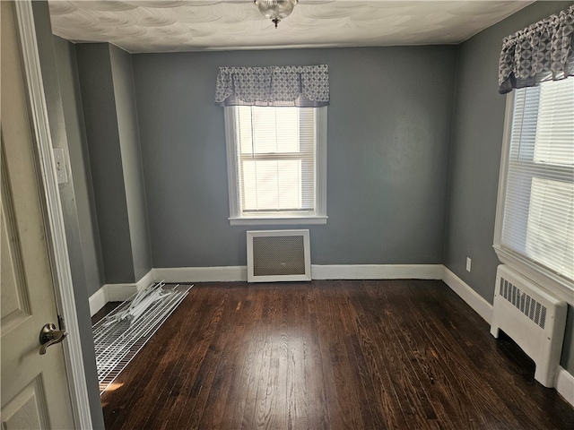 spare room featuring dark hardwood / wood-style flooring, radiator heating unit, and a wealth of natural light