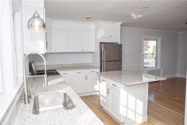 kitchen featuring hanging light fixtures, light stone countertops, light wood-type flooring, a kitchen island, and stainless steel refrigerator