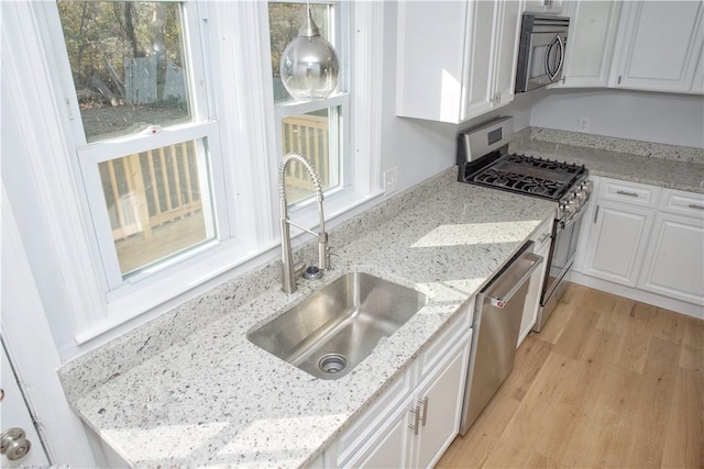 kitchen featuring sink, light stone countertops, light hardwood / wood-style floors, white cabinetry, and stainless steel appliances