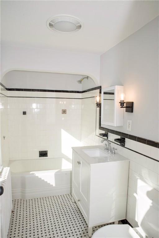 bathroom featuring radiator, vanity, tiled shower / bath combo, and tile walls