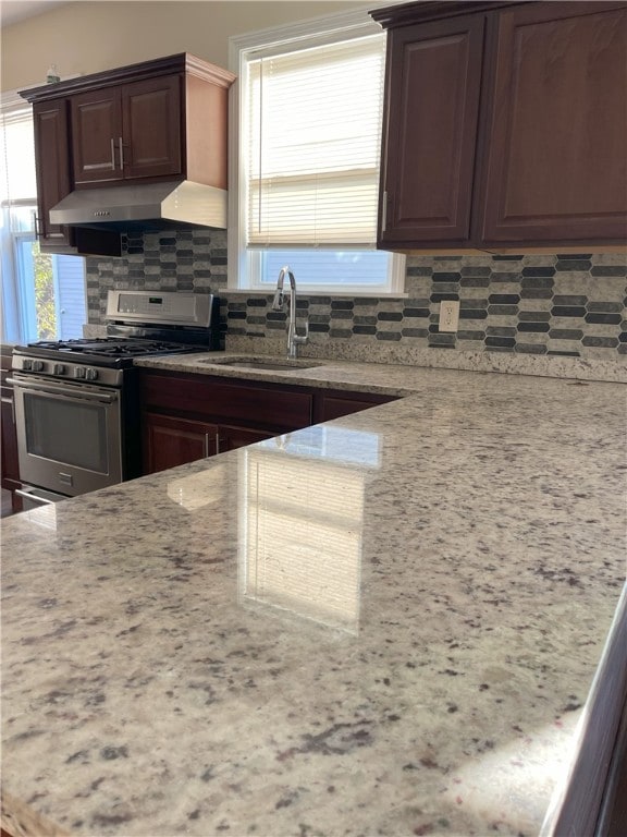 kitchen featuring stainless steel gas range, sink, backsplash, light stone counters, and dark brown cabinets