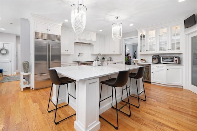 kitchen featuring a breakfast bar, light hardwood / wood-style floors, white cabinetry, hanging light fixtures, and built in fridge