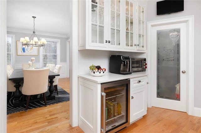 bar with beverage cooler, decorative light fixtures, light hardwood / wood-style flooring, a chandelier, and white cabinetry