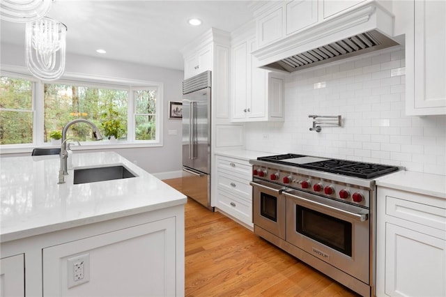 kitchen featuring light wood-type flooring, premium range hood, premium appliances, sink, and white cabinetry