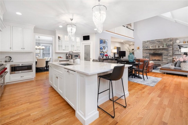 kitchen with white cabinets, light hardwood / wood-style floors, a stone fireplace, and sink